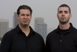 Two Happy Men in Black Shirts Pose in Front of Skyscraper