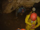 Exploring the Depths Caption: Two workers don their hardhats to venture into the depths of a cave, surrounded by the rugged beauty of nature's rocks.