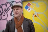 Man in Hat and Scarf in Front of Colorful Building