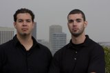 Two Men in Black Shirts Posing in Front of Skyscraper