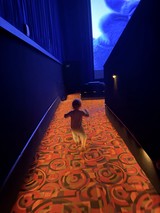 Child Running Through Illuminated Carpet Hallway in Dark Museum
