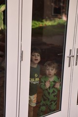 Two Children Peering Through Glass Door at Home