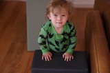 Toddler in Green Dinosaur Pajamas on Brown Couch