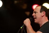 Rocking the Crowd Caption: A male singer performs at a concert, singing into a microphone while bathed in the spotlight and surrounded by an enthusiastic crowd.