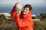 Woman Playfully Holds Giant Rock by the Sea
