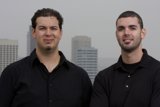 Two Happy Men in Black Shirts Pose in Front of Skyscraper