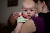 Wide-Eyed Baby Gazes Curiously Over Mother's Shoulder