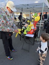 Balloon Artist Delights Young Child at Farmers Market