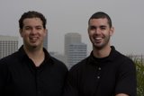Smiling Duo in Black Shirts Pose Against a Skyscraper
