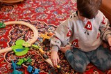 Child Playing with Wooden Train Set on Patterned Rug