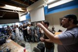 Man Speaks to Audience in Plywood-Finished Room