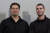 Two Happy Men in Black Shirts Pose in front of Skyscraper