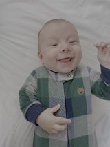 Smiling Baby in Plaid Sleeper on White Bedding