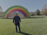 Man Poses by Large Rainbow Art Installation