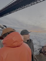 Boat Passengers Under Suspension Bridge at Dusk