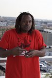 Smiling Man in Red T-Shirt Poses in Front of Buildings and Cars