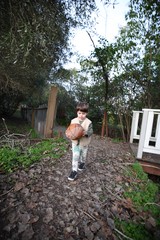Young Boy Carrying Basketball Through Garden Path