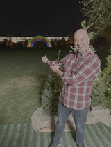 Man Celebrates with Trophy Under Rainbow