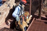 A Woman in Hard Hat and Harness Scaling a Rocky Path
