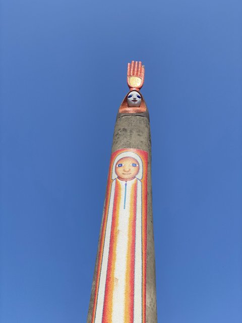Painted Face Totem Pole Against Clock Tower