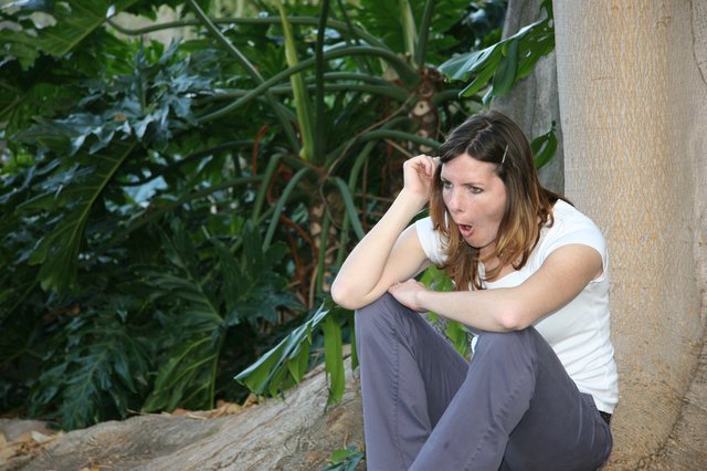Surprised Woman Crouching by Tropical Garden Wall