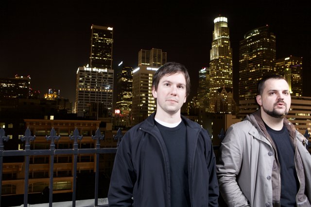 Two Men in Overcoats Stand before a Metropolitan Skyline