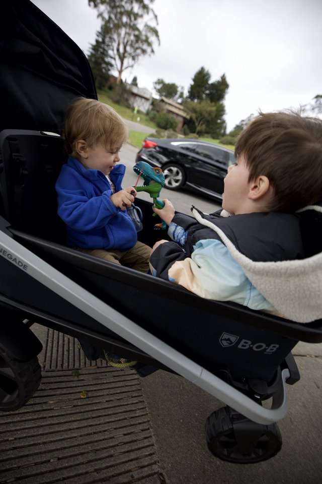 Two Young Children Sharing Toys in Double Stroller