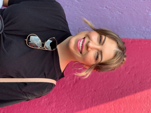 Smiling Woman in Sunglasses Poses in Front of Colorful Wall