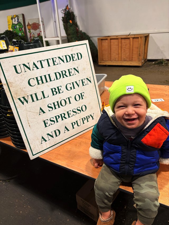 Joyful Toddler at Coffee Shop with Humorous Warning Sign