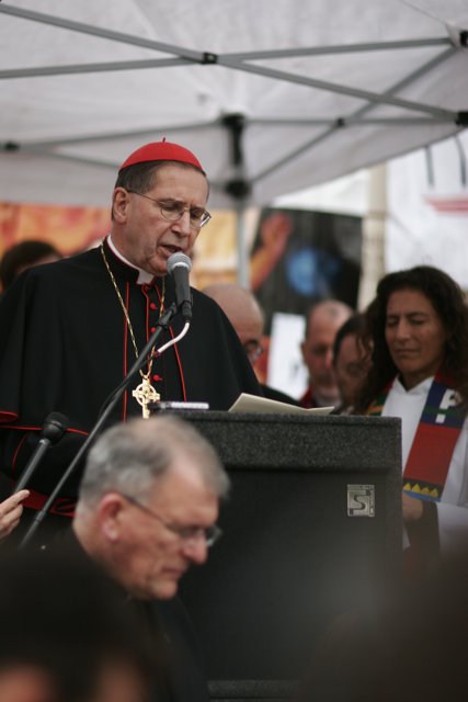 Red-Hatted Bishop Addresses Crowd at Podium