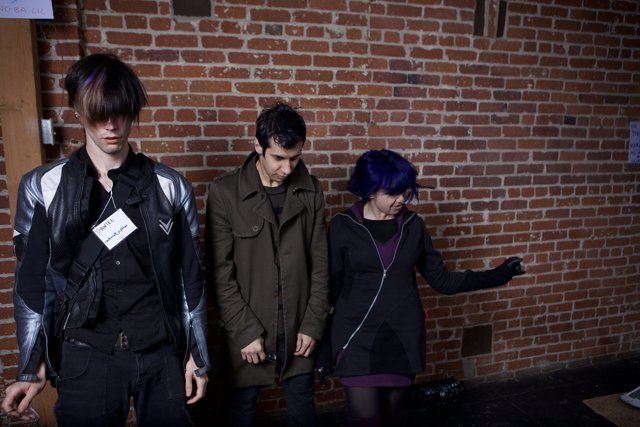 Three Adults in Jackets Standing by Brick Wall