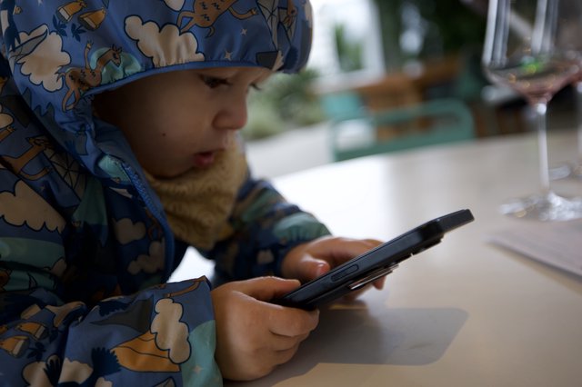 Young Child Engaged with Smartphone at Restaurant