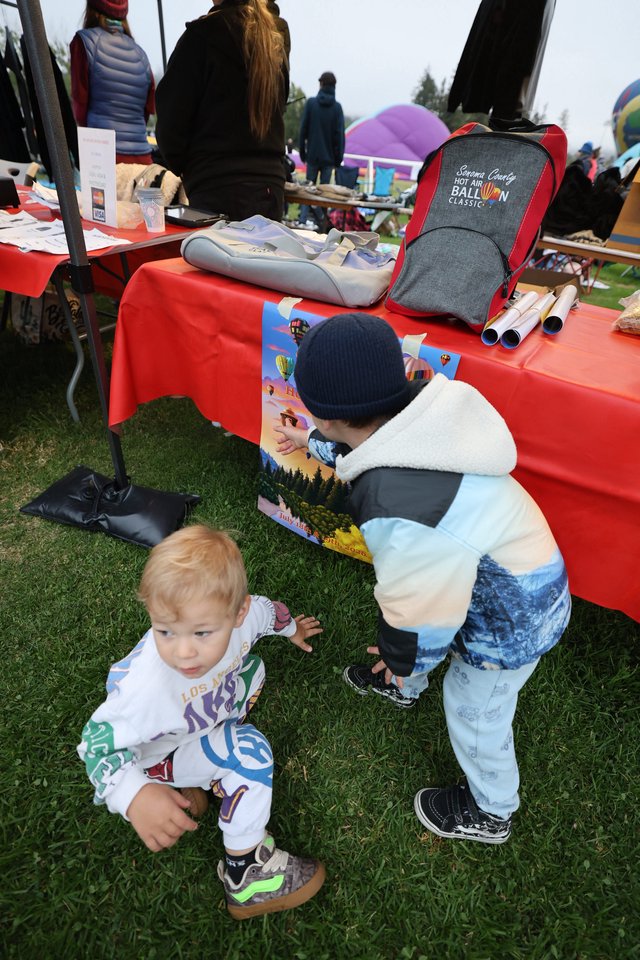 Curious Toddlers Explore Balloon Festival Merchandise Table