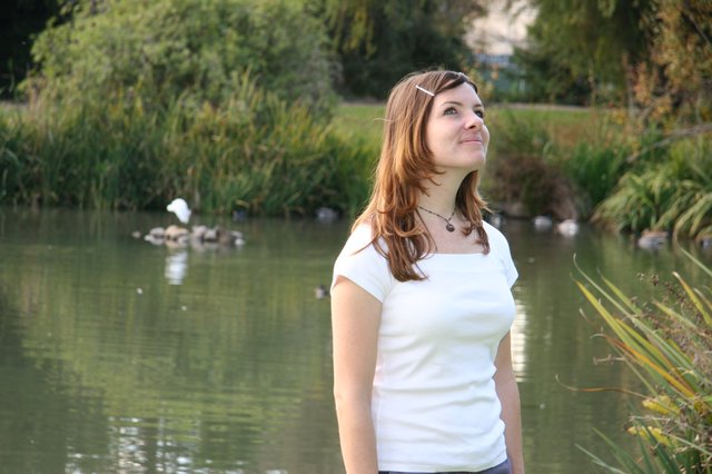 Young Woman Gazing Upward by a Peaceful Park Pond
