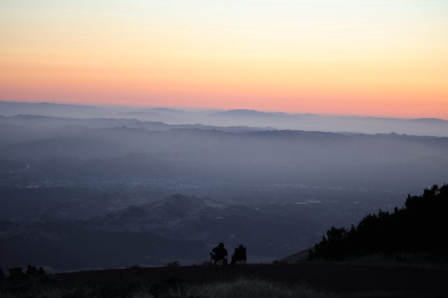 Two Silhouettes Watching Sunset Over Layered Mountain Valleys