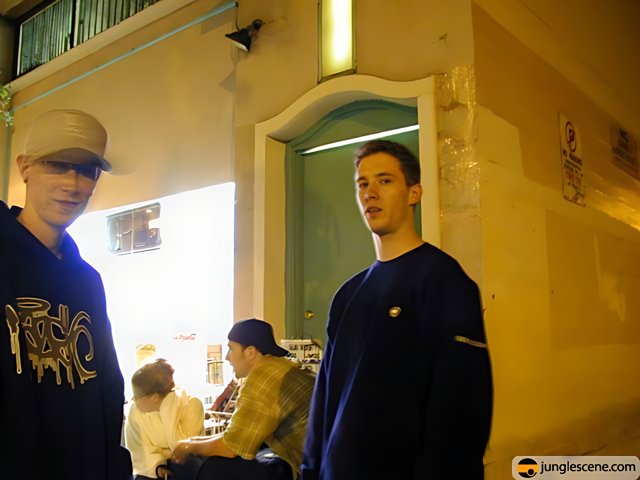 Two Men in Hats Pose in Front of Building at Night