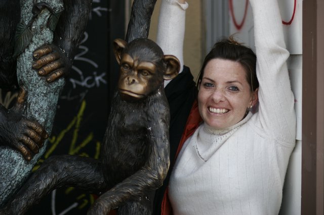 Woman Poses Playfully Beside Bronze Chimp Sculpture