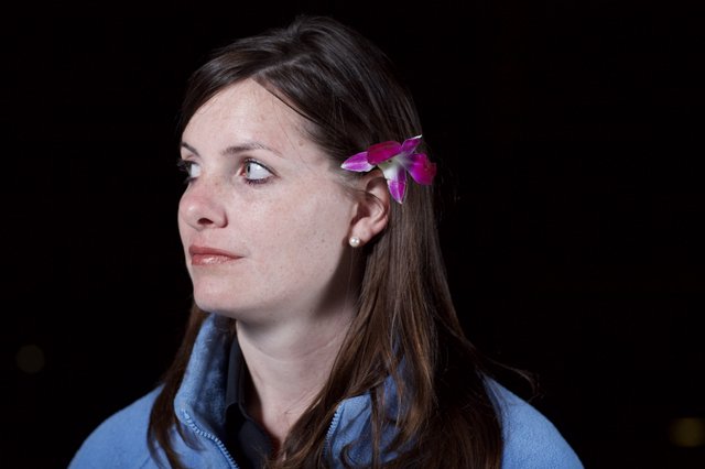 Woman with Orchid in Hair Against Dark Background