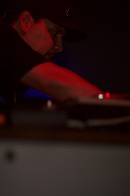 The DJ in the Black Hat Caption: This man, wearing a black shirt and hat, expertly spins tracks to keep the crowd moving at the nightclub.