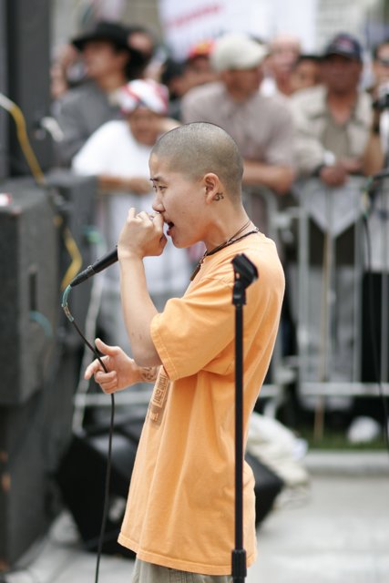 Man with Orange Shirt Speaking into Microphone