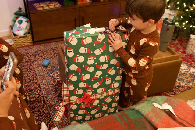 Christmas Morning: Child Unwrapping Santa-Themed Present