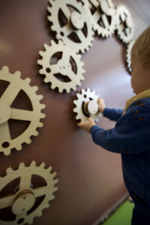 Child Playing with Wooden Gear Wall Installation