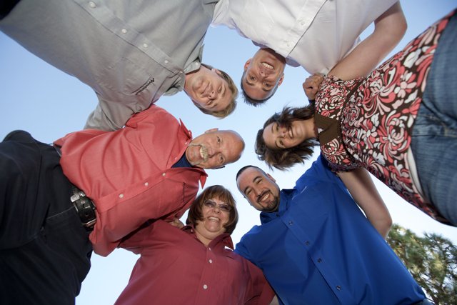 Circle of Friends Caption: Eight people, three women and four men, wearing a mix of casual and formal clothing, huddle together under a bright blue sky.