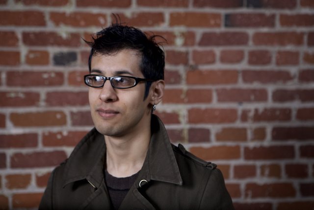 Smiling Man in Jacket and Glasses Poses by Brick Wall