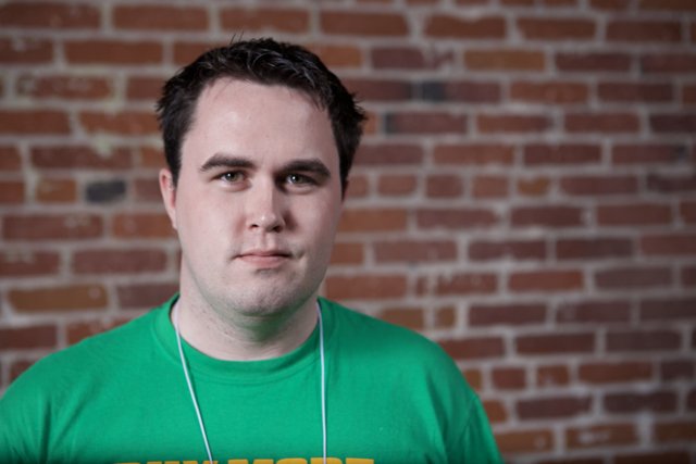 Man in Green T-Shirt Poses Against Brick Wall