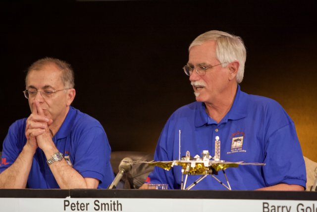 NASA Director Charles Elachi Discusses Phoenix Landing Caption: NASA Director Charles Elachi speaks at a press conference, using a microphone to discuss the Phoenix landing and pointing towards the space shuttle at the table in front of him, while another man listens attentively.