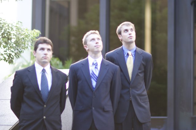 Three Men in Suits Pose in Front of Building