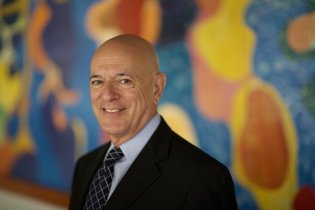 Bald Man in Suit and Tie Stands in Front of Colorful Painting