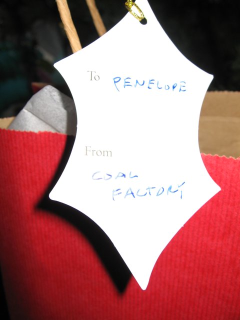 Reupli Gift Bag Caption: A red gift bag with a to reupli from coal palace tag, captured on December 24th, 2005 at 2:08 pm. The handwriting on the tag adds a personal touch to the festive symbol.
