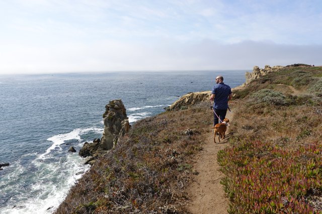 Man and His Dog Enjoying a Hike on a Promontory Trail